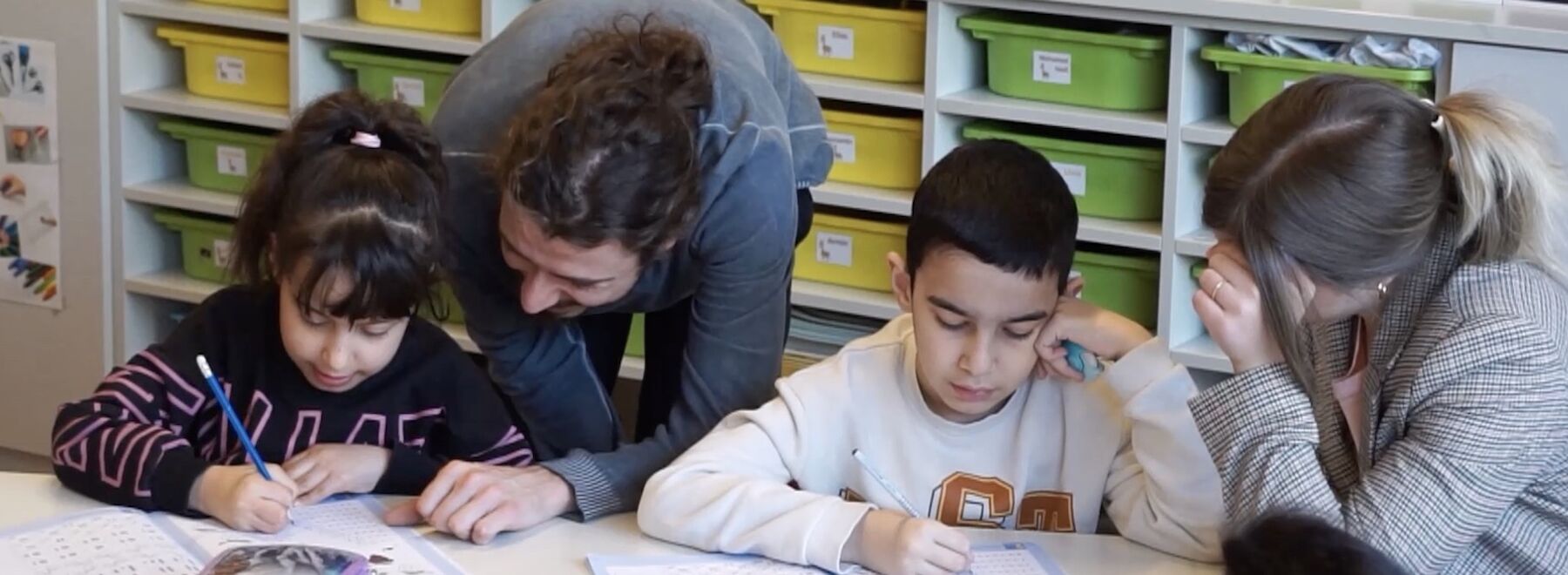 Zwei Studierende helfen zwei Schüler*innen in der Klasse