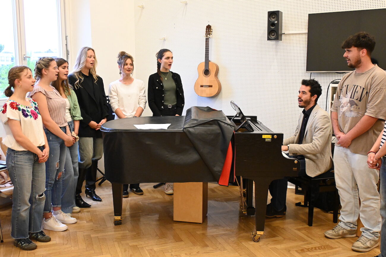 Studierende und Lehrender im Musikraum beim Klavier