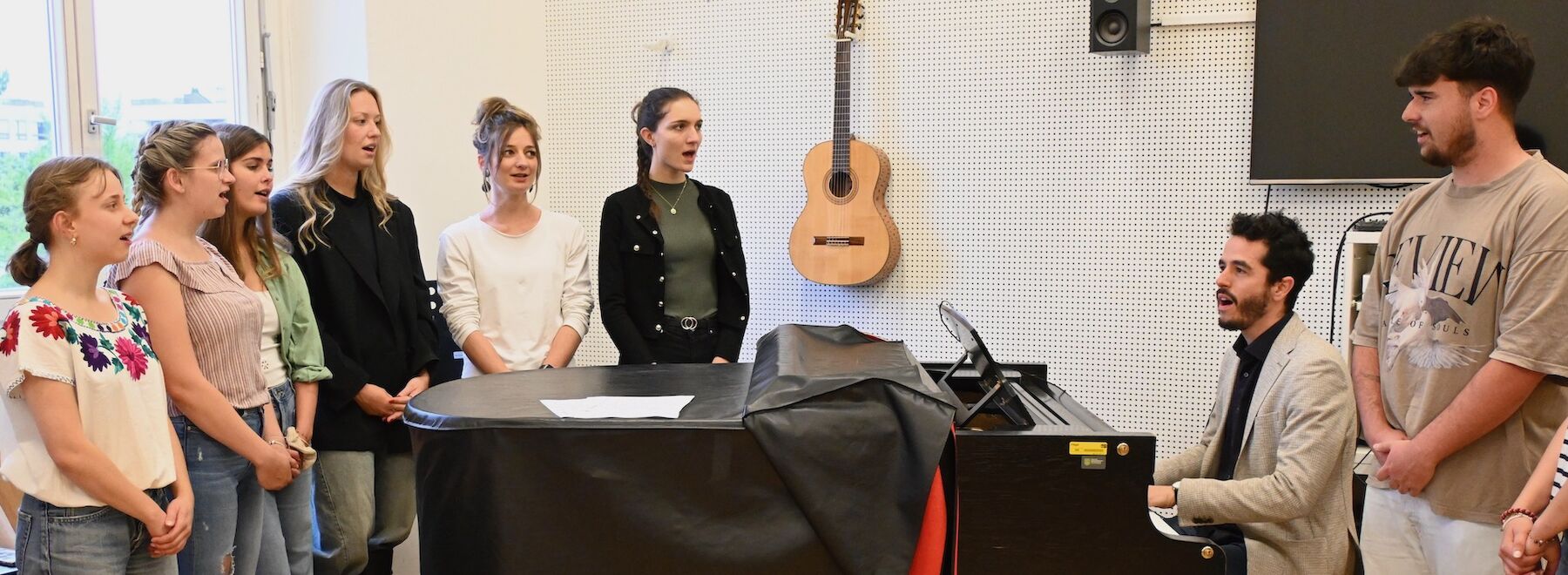Studierende und Lehrender im Musikraum beim Klavier