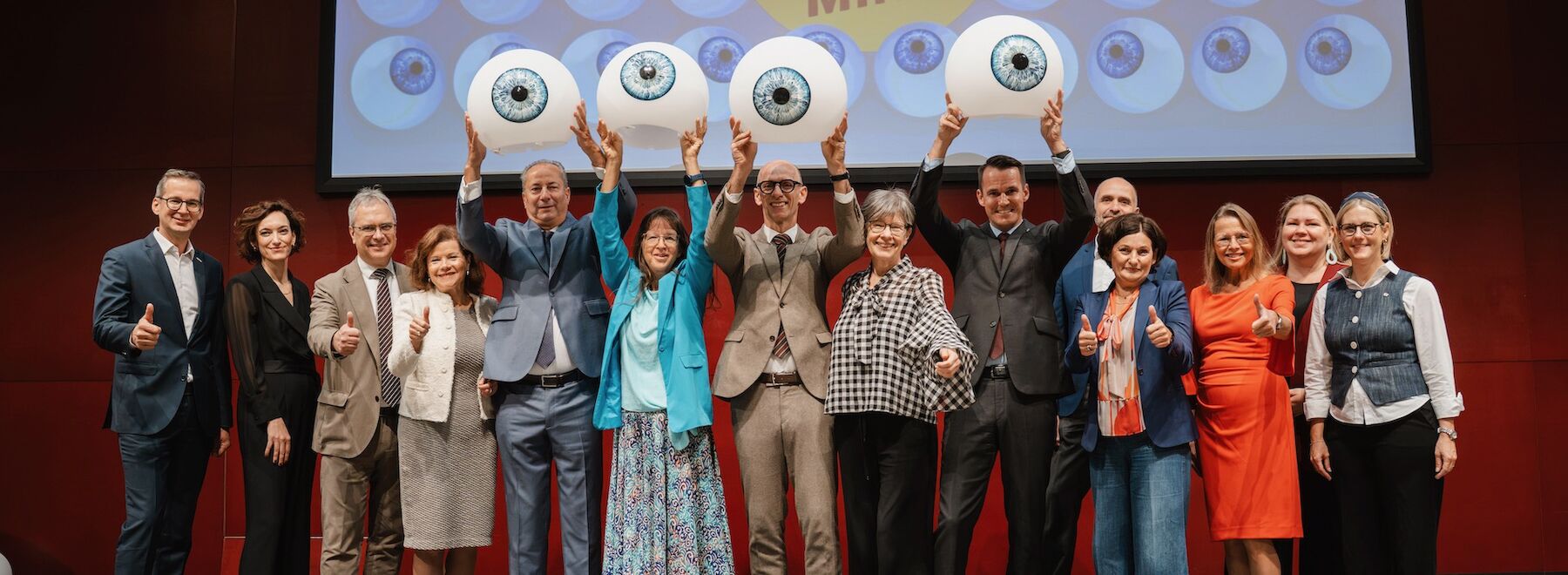 Gruppenbild: Verantwortliche MINT Festival im Festsaal mit dekorativen großen Augen in den Händen haltend