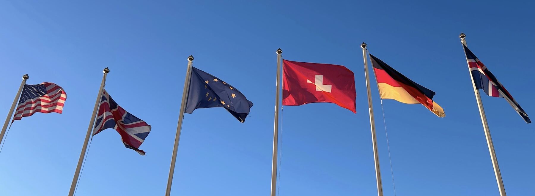 Fünf nordische Länderflaggen auf Fahnenmasten vor einem blauen Himmel mit Wolken.