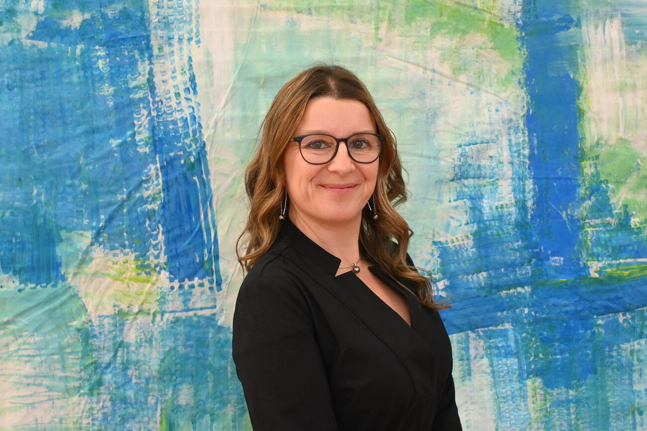 Lächelnde Frau mit Brille im Herbstpark, trägt einen gemusterten Schal.