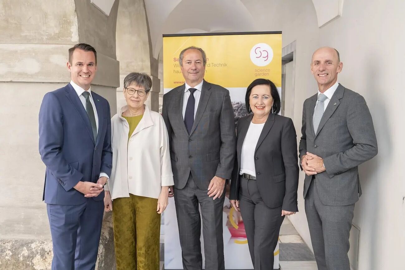 Fünf professionell gekleidete Menschen stehen lächelnd vor einem Banner.
