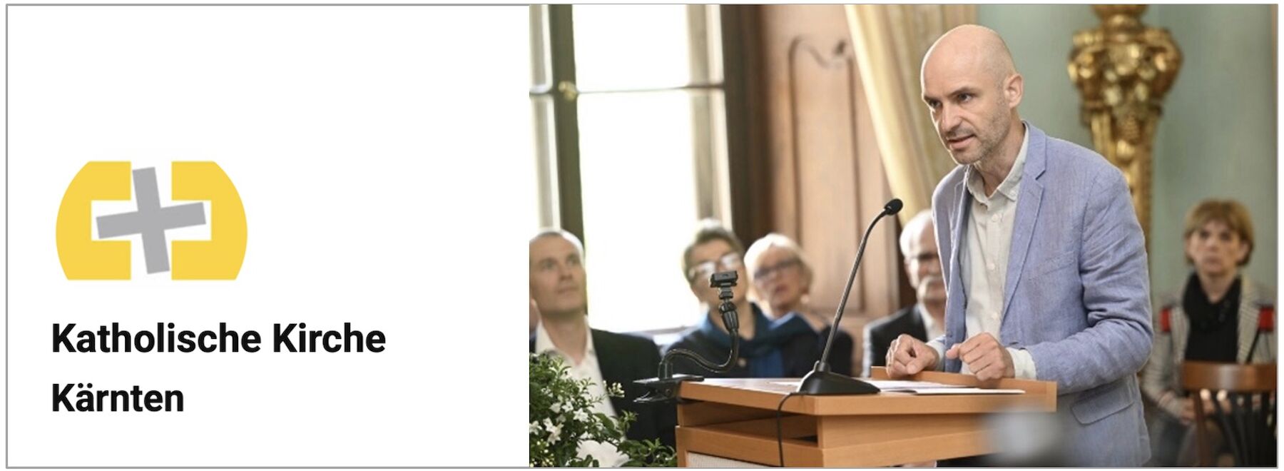 Mann spricht an einem Podium in einer Kirche; links Logo der Katholischen Kirche Kärnten.