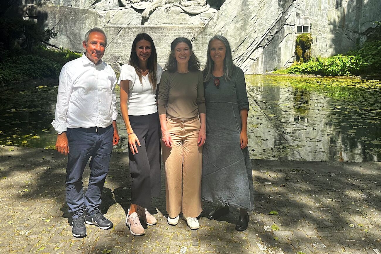 Vier Menschen stehen lächelnd vor einem Teich und einem großen Steindenkmal im Freien.