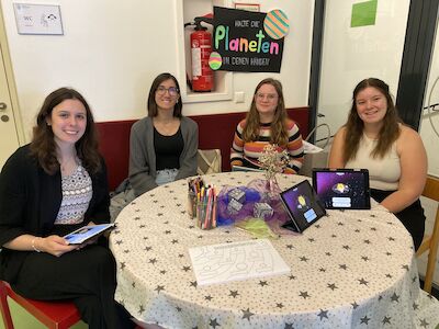 Vier junge Frauen sitzen mit Malutensilien und Tablets an einem runden Tisch.