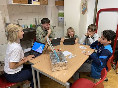 Fünf Schüler sitzen in einem Klassenzimmer um einen Tisch und arbeiten an Laptops und Tablets.