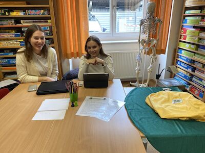 Zwei Frauen sitzen mit Tablets an einem Tisch in einem Raum voller Brettspiele.