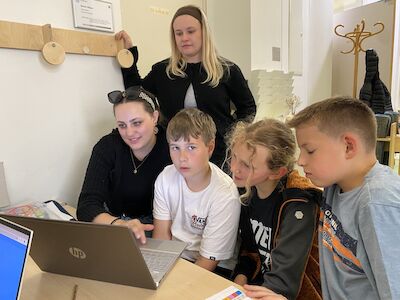 Vier Kinder und zwei Erwachsene schauen gemeinsam in einem Klassenzimmer auf einen Laptop.