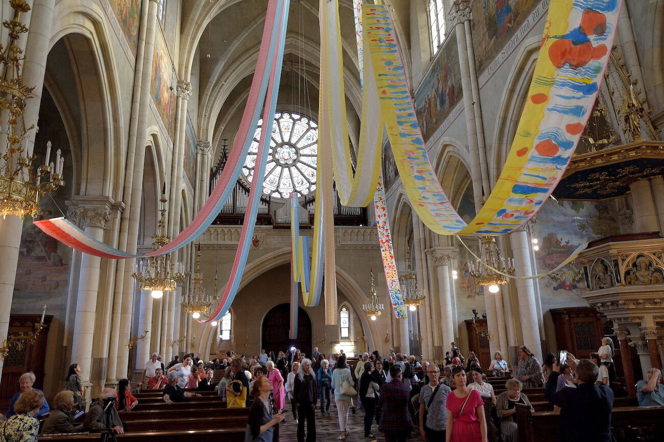 Bunte Stoffbahnen ziehen sich in einer Kirche von der Decke bis zum Boden.