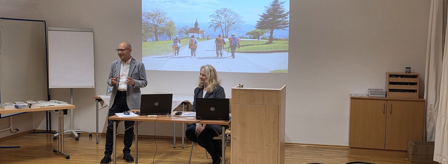 Zwei Lehrende im Seminarraum vor einer Wandprojektion